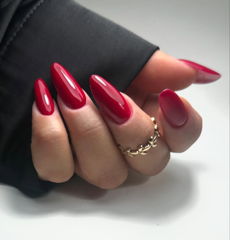 Hand with red nail polish wearing a gold ring on a neutral background