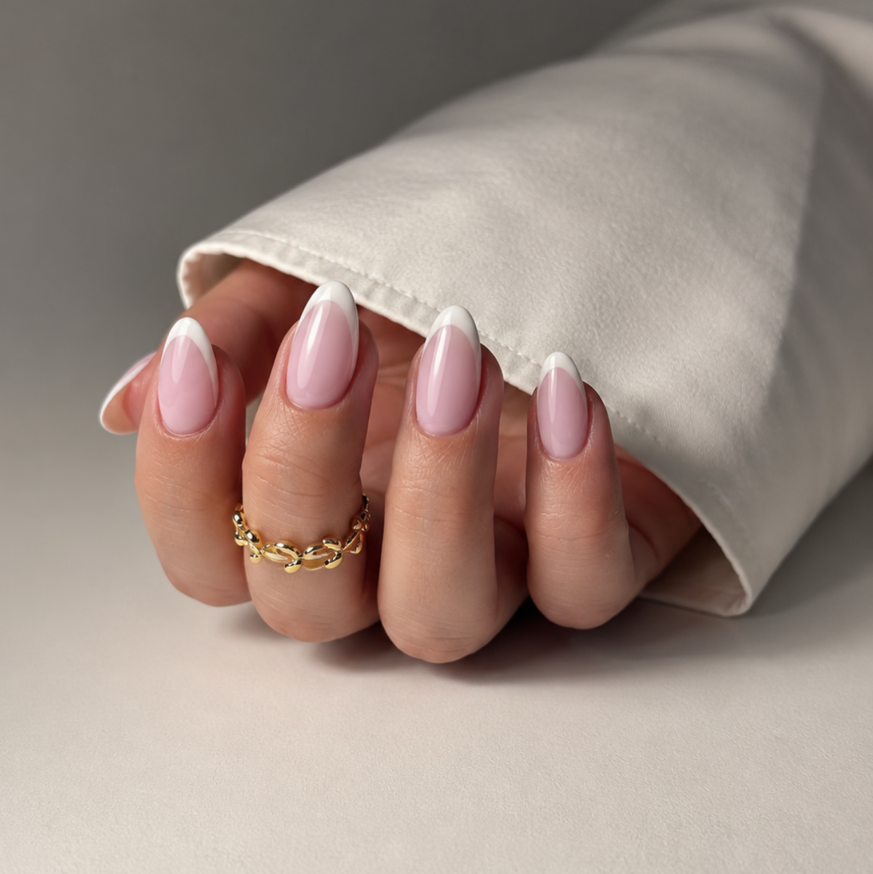 Hand with pink nail polish and a gold ring on a neutral background